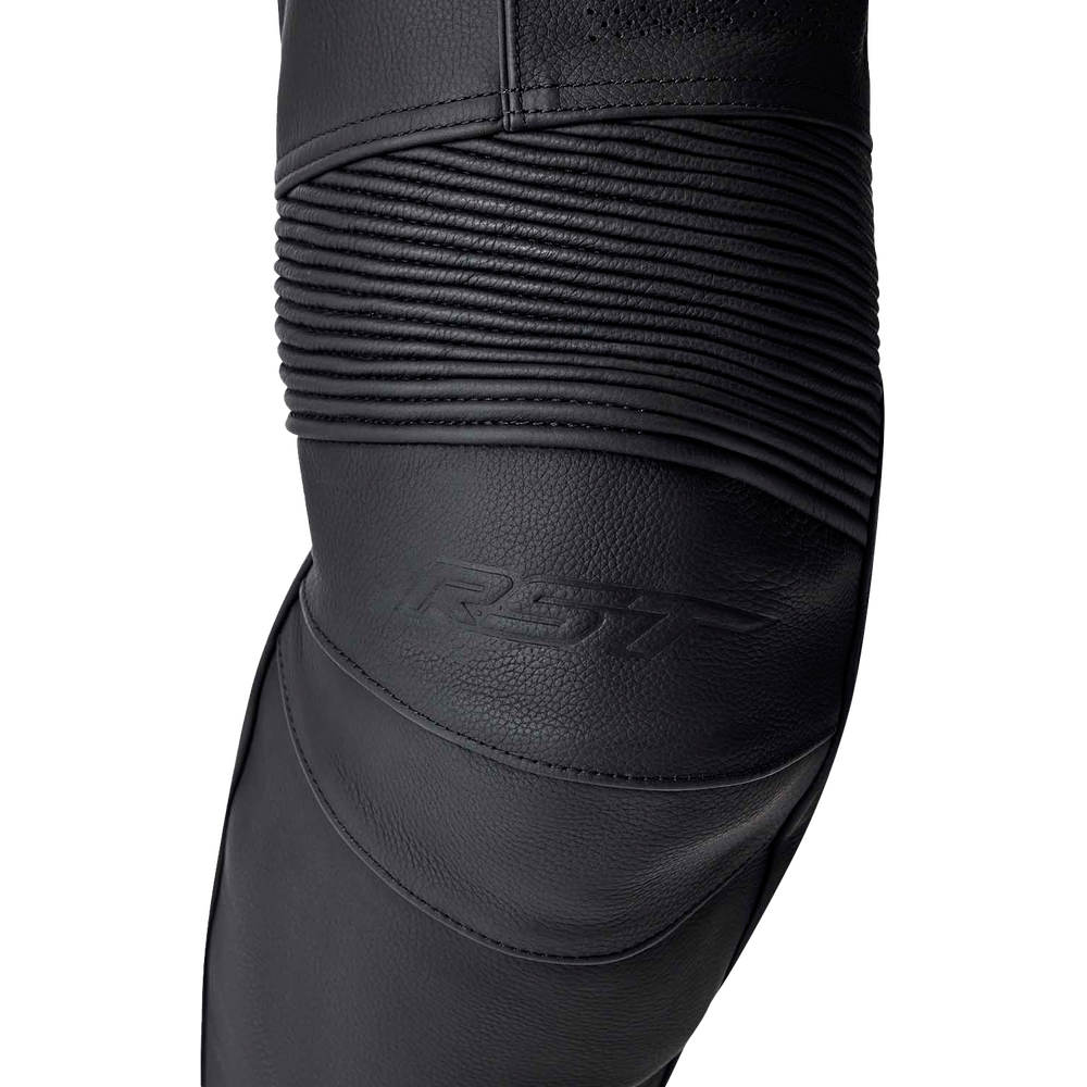 Close-up of a black motorcycle leather leg warmer or knee protector with textured panels and a ribbed section, featuring an embossed RST logo, on a white background.