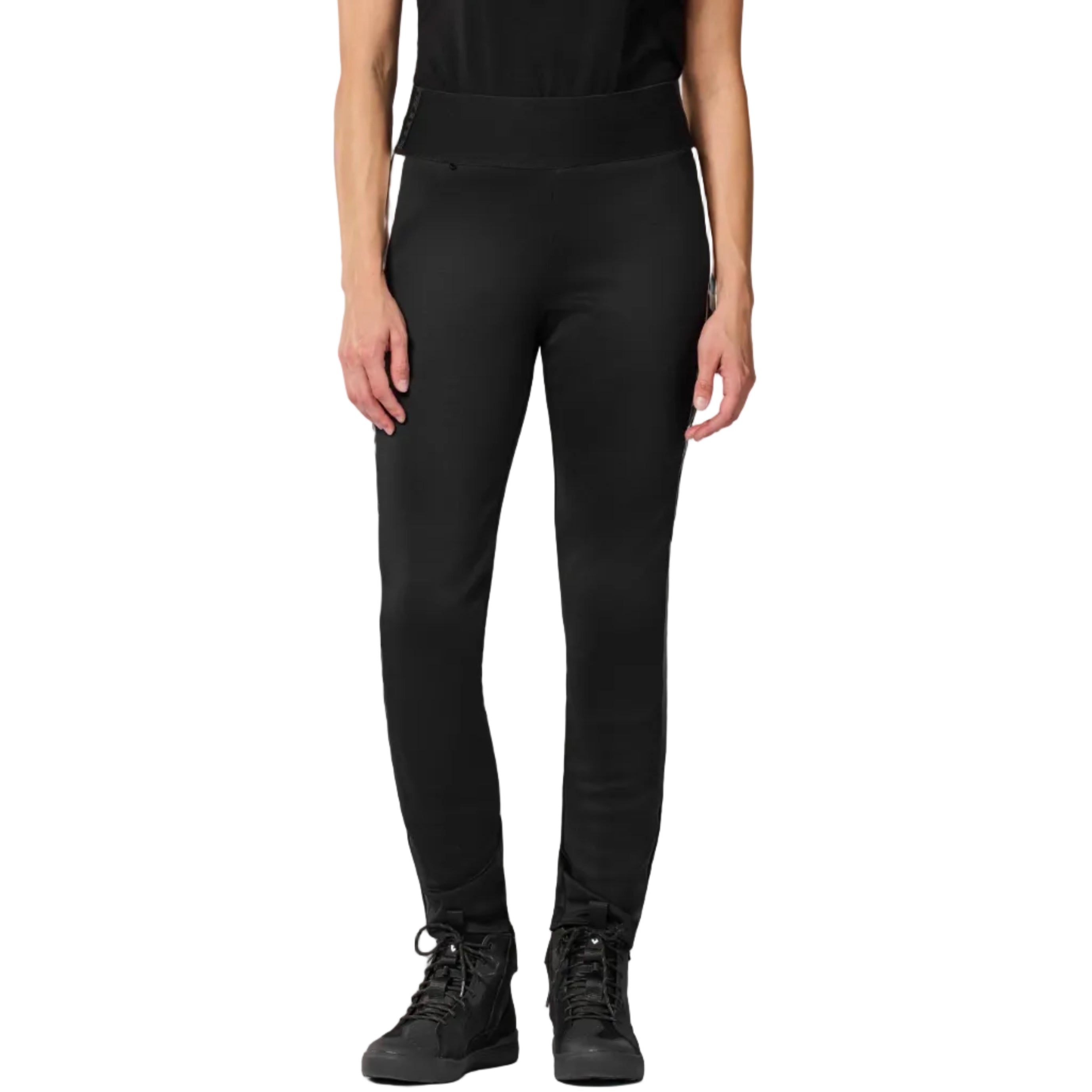 A model from the waist down wearing black athletic leggings and black lace-up sneakers, standing against a light off-white studio background.