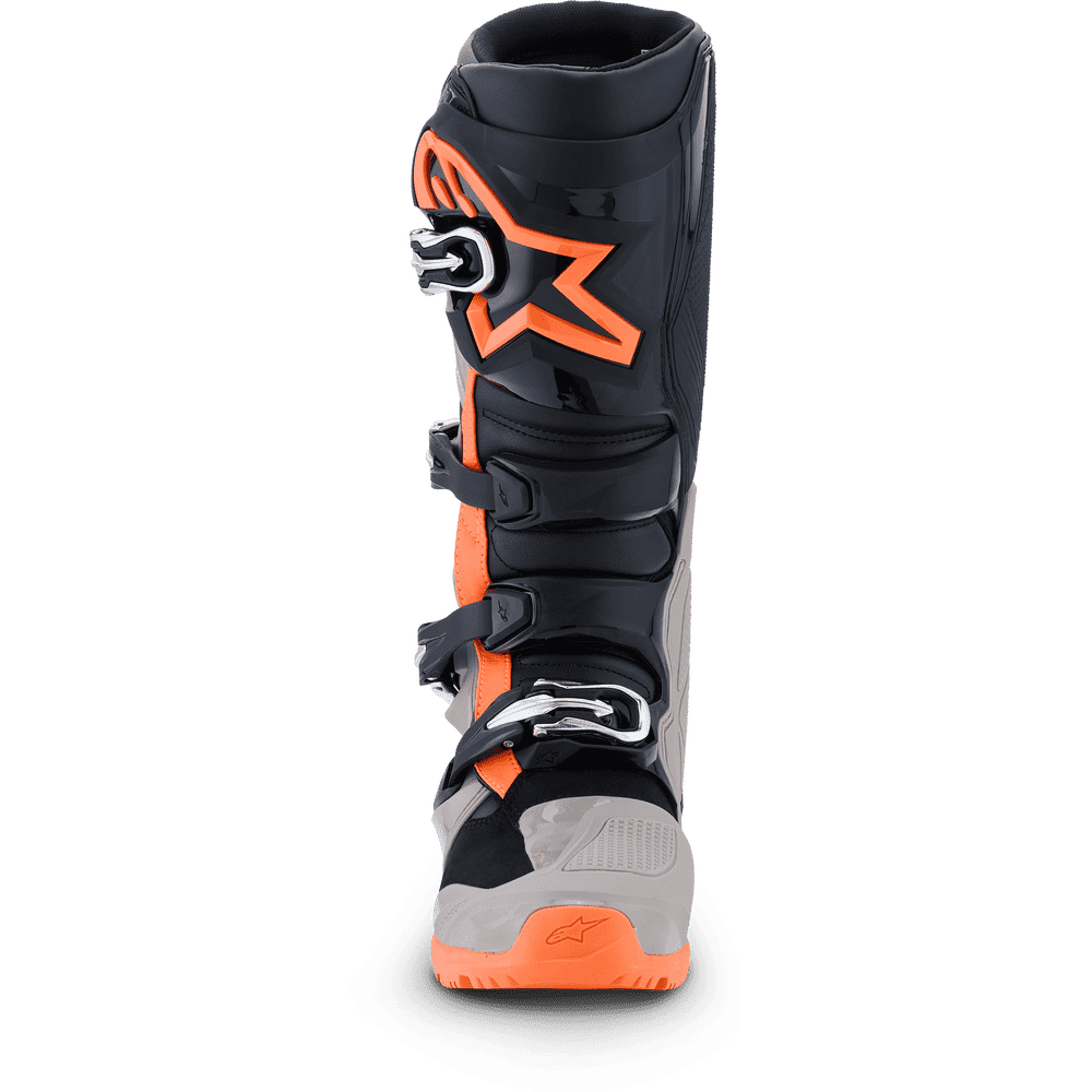 A single Alpinestars motocross boot shown from the rear three-quarter view, featuring a black upper with a prominent orange star logo, orange accents, gray heel and toe areas, and silver buckle closures.