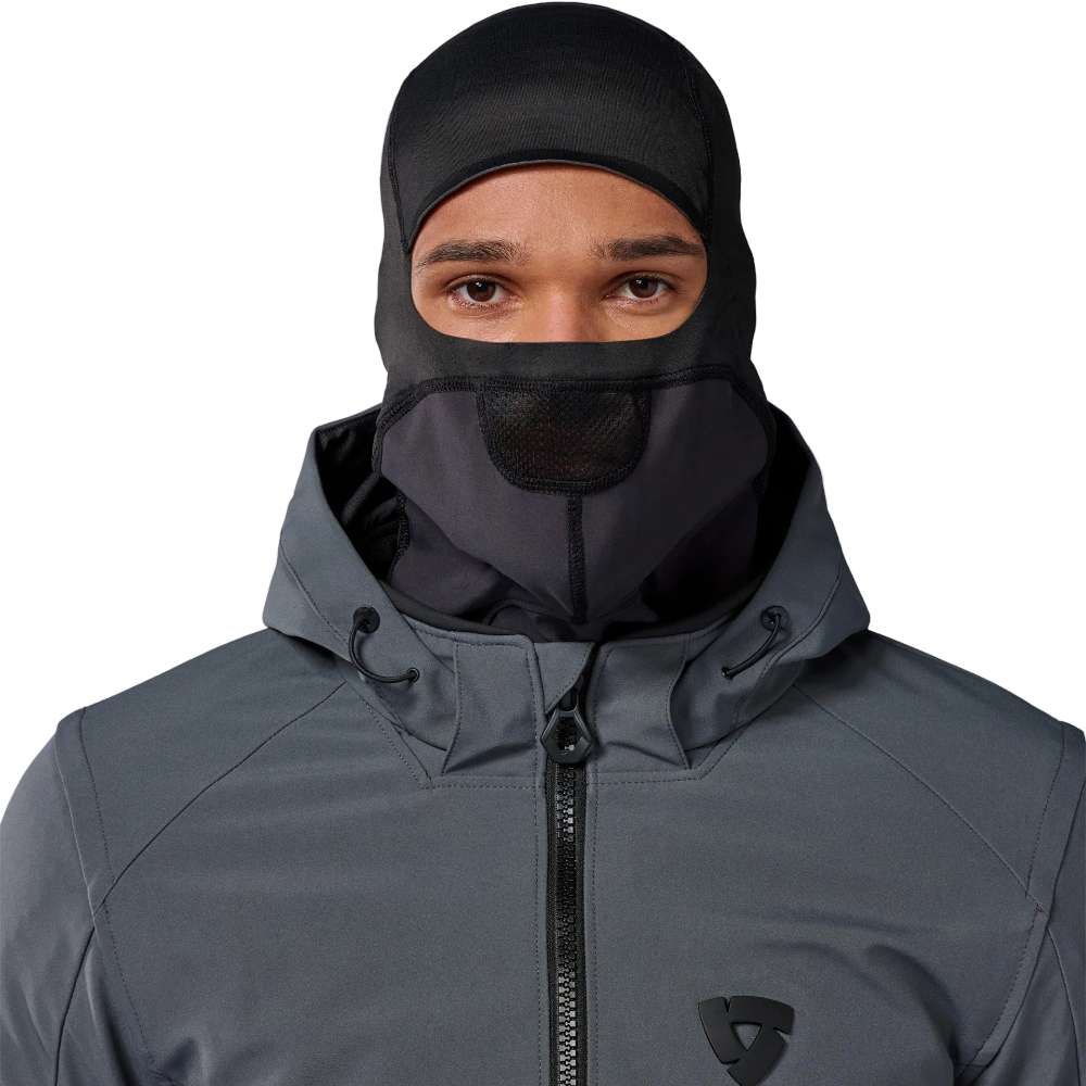 A man wearing a dark gray hooded technical jacket and a black balaclava face mask, shown from the chest up against a plain light background.